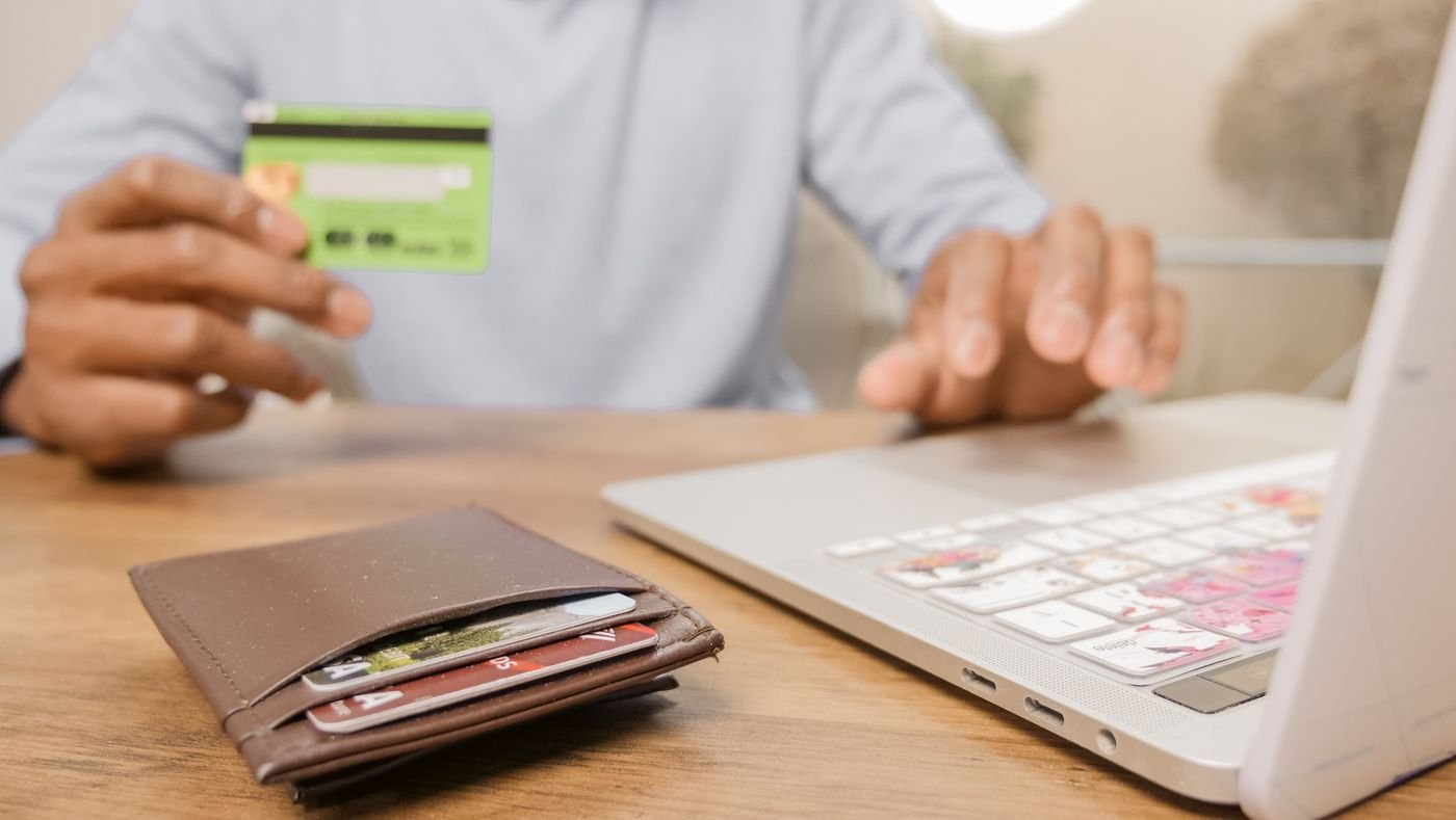 Manos sosteniendo una tarjeta bancaria frente a una computadora portátil